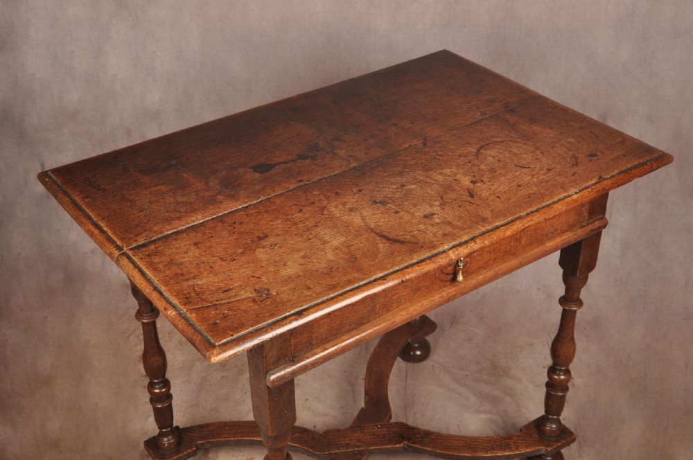 A 17th-century oak side table featuring baluster-turned legs, a shaped X-stretcher, a single frieze drawer with a brass drop handle, and a rectangular timber top. View X