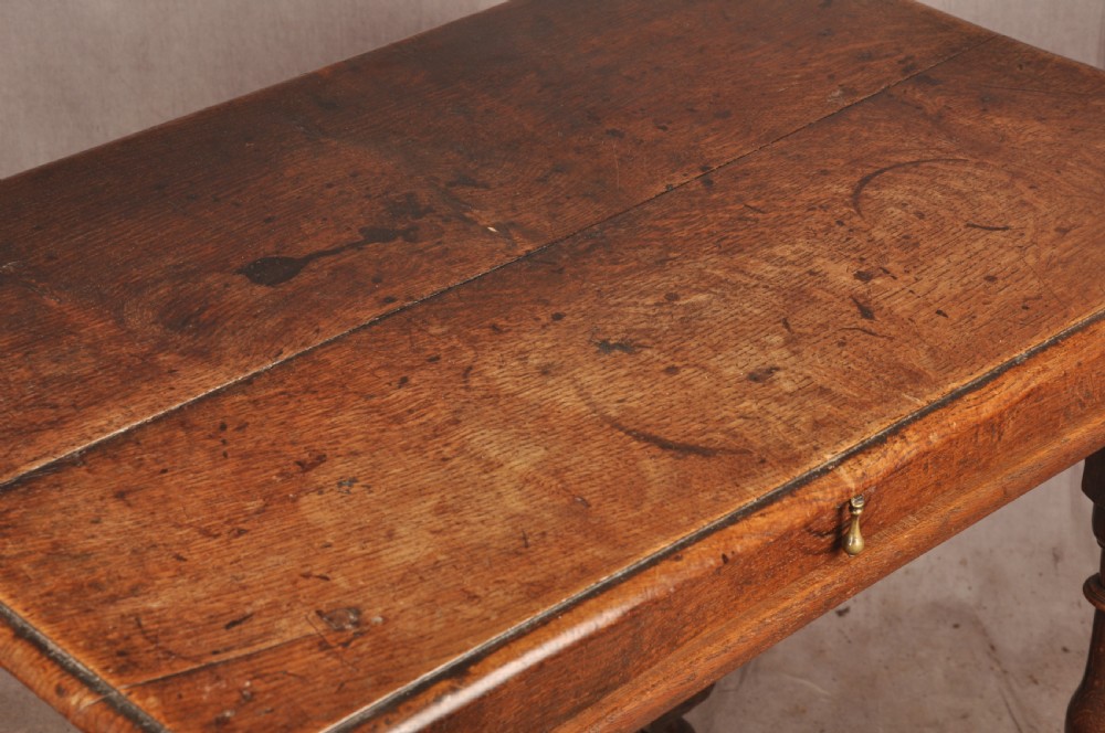 A 17th-century oak side table featuring baluster-turned legs, a shaped X-stretcher, a single frieze drawer with a brass drop handle, and a rectangular timber top. View XI
