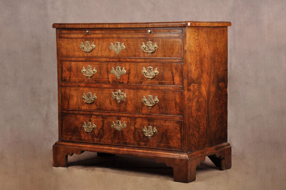 A George II walnut chest of drawers featuring four graduated drawers with brass handles and escutcheons, resting on bracket feet.