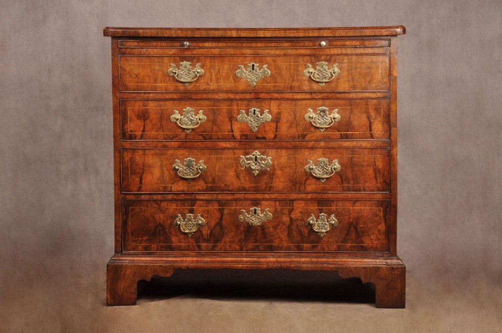 A George II walnut chest of drawers featuring four graduated drawers with brass handles and escutcheons, resting on bracket feet. View II