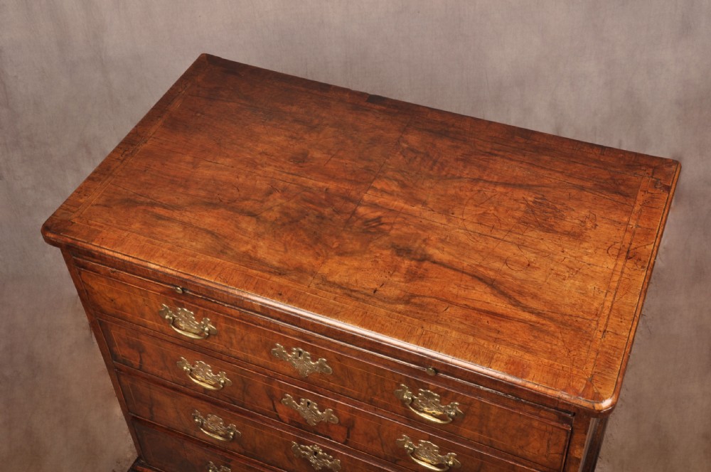 A George II walnut chest of drawers featuring four graduated drawers with brass handles and escutcheons, resting on bracket feet. View III