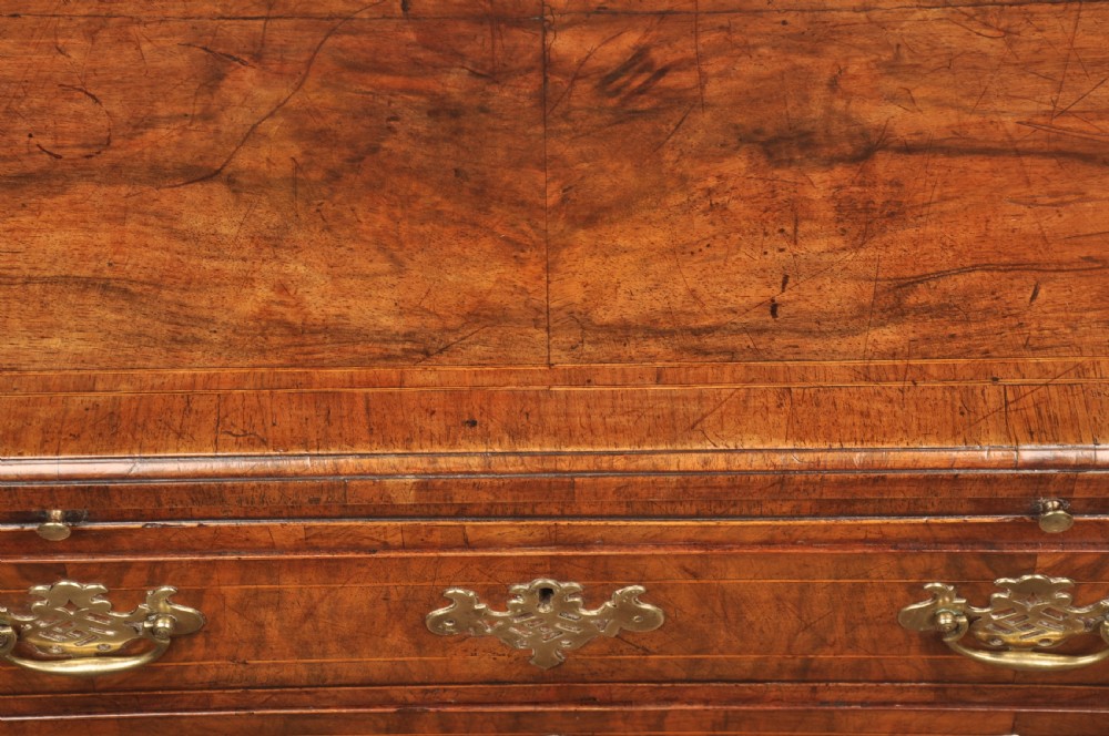 A George II walnut chest of drawers featuring four graduated drawers with brass handles and escutcheons, resting on bracket feet. View IV