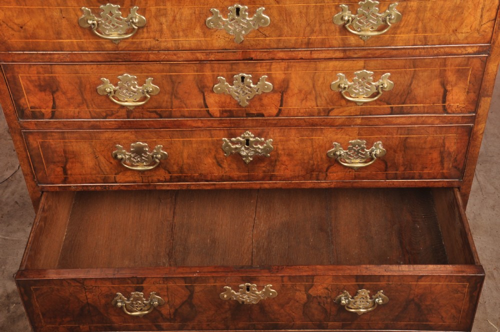 A George II walnut chest of drawers featuring four graduated drawers with brass handles and escutcheons, resting on bracket feet. View V