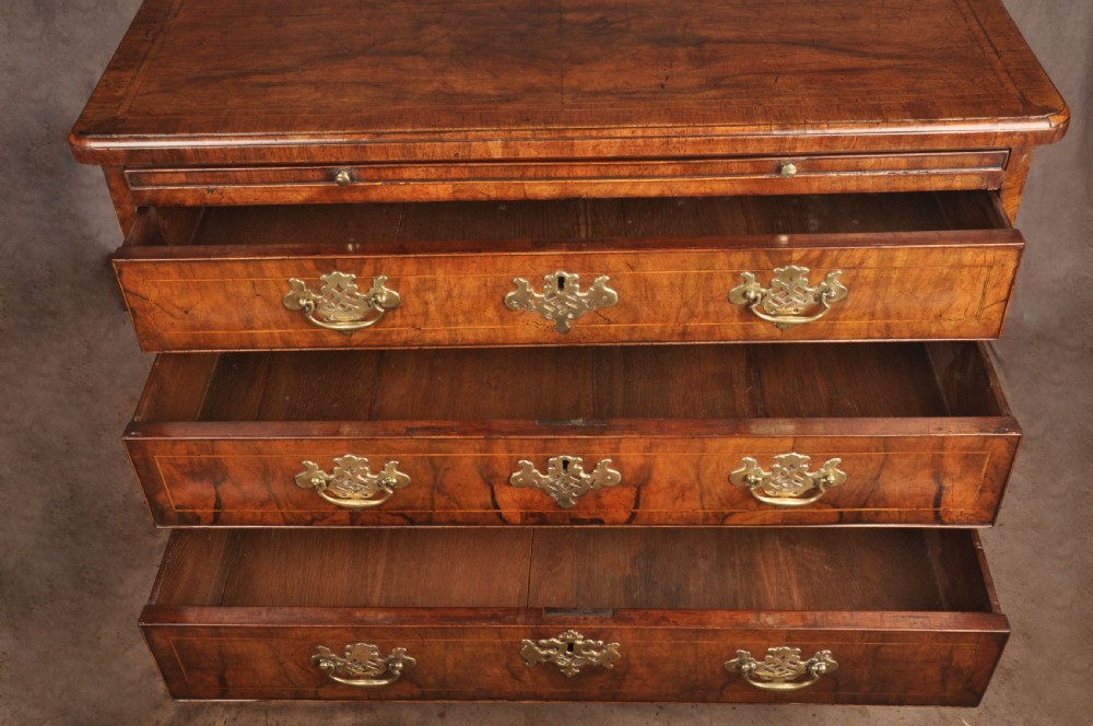 A George II walnut chest of drawers featuring four graduated drawers with brass handles and escutcheons, resting on bracket feet. View VI