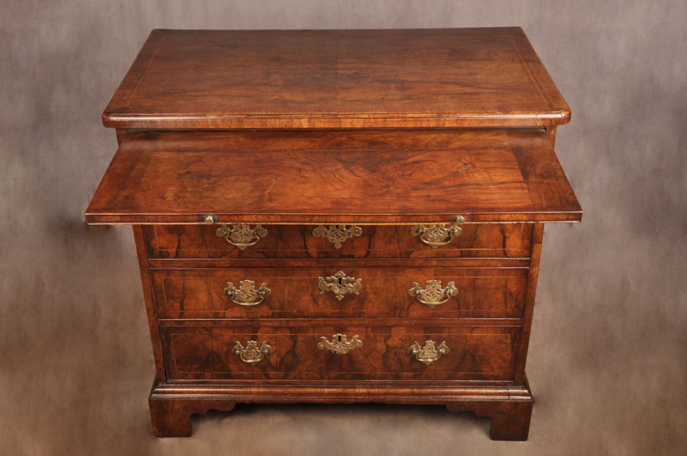 A George II walnut chest of drawers featuring four graduated drawers with brass handles and escutcheons, resting on bracket feet. View VII