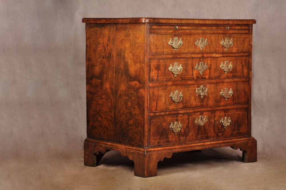 A George II walnut chest of drawers featuring four graduated drawers with brass handles and escutcheons, resting on bracket feet. View XI