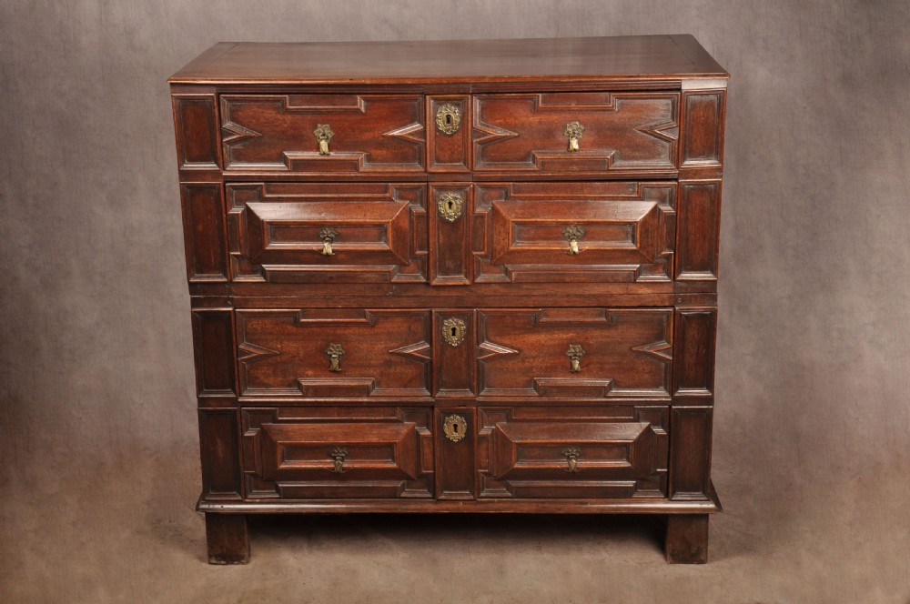 A 17th-century Charles II walnut and fruitwood chest of drawers featuring geometric mitred panels and brass keyhole escutcheons.