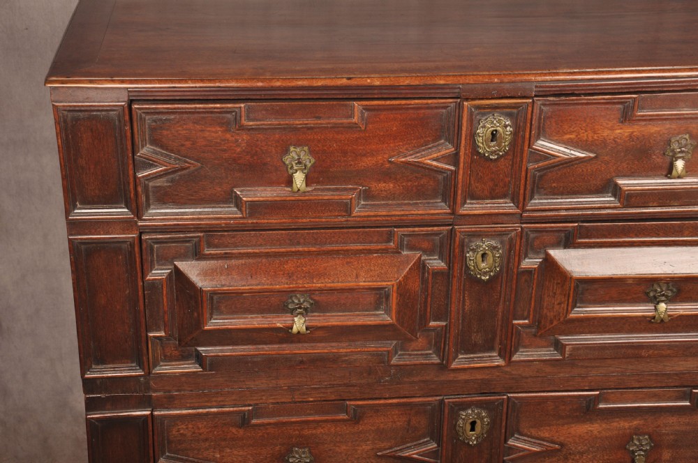 A 17th-century Charles II walnut and fruitwood chest of drawers featuring geometric mitred panels and brass keyhole escutcheons. View IV