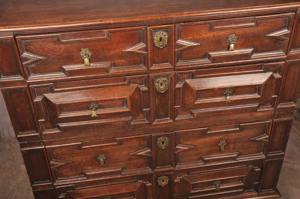 A 17th-century Charles II walnut and fruitwood chest of drawers featuring geometric mitred panels and brass keyhole escutcheons. View V