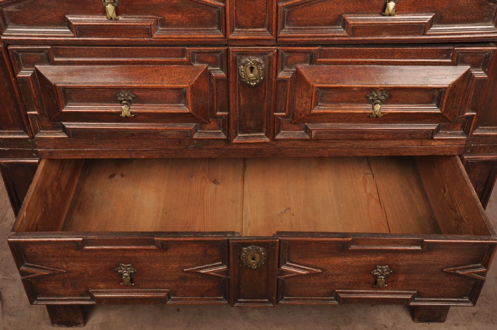A 17th-century Charles II walnut and fruitwood chest of drawers featuring geometric mitred panels and brass keyhole escutcheons. View XI