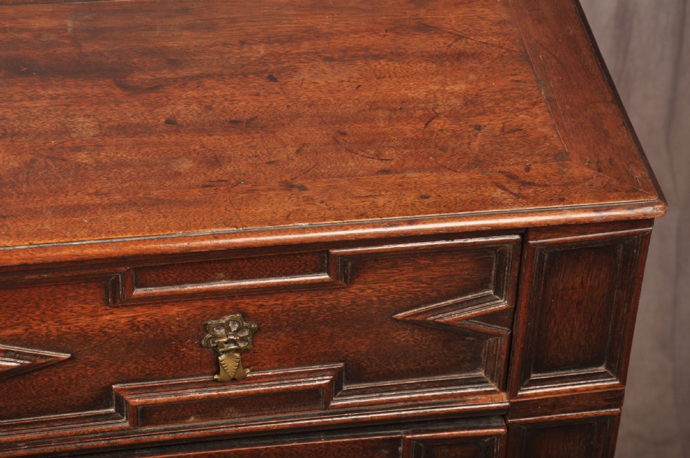A 17th-century Charles II walnut and fruitwood chest of drawers featuring geometric mitred panels and brass keyhole escutcheons. View XIV