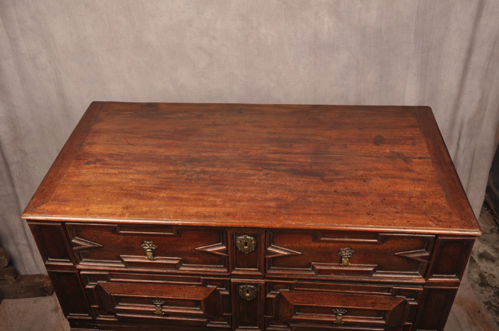 A 17th-century Charles II walnut and fruitwood chest of drawers featuring geometric mitred panels and brass keyhole escutcheons. View XV