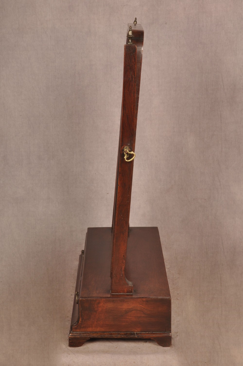 An 18th-century mahogany toilet mirror featuring an adjustable glass plate surrounded by a gilt slip, supported by vertical uprights with brass finials over a single-drawer plinth base. View II