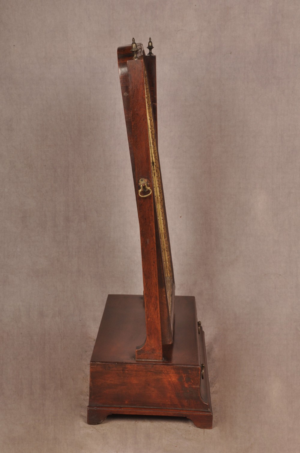 An 18th-century mahogany toilet mirror featuring an adjustable glass plate surrounded by a gilt slip, supported by vertical uprights with brass finials over a single-drawer plinth base. View III