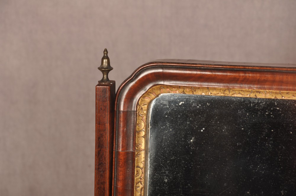 An 18th-century mahogany toilet mirror featuring an adjustable glass plate surrounded by a gilt slip, supported by vertical uprights with brass finials over a single-drawer plinth base. View V