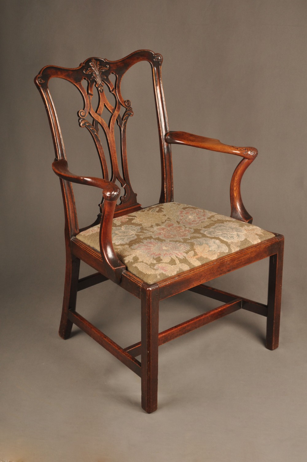 An 18th-century Chippendale mahogany armchair featuring a carved pierced splat back, swept armrests, an upholstered drop-in seat, and square legs joined by H-stretchers.