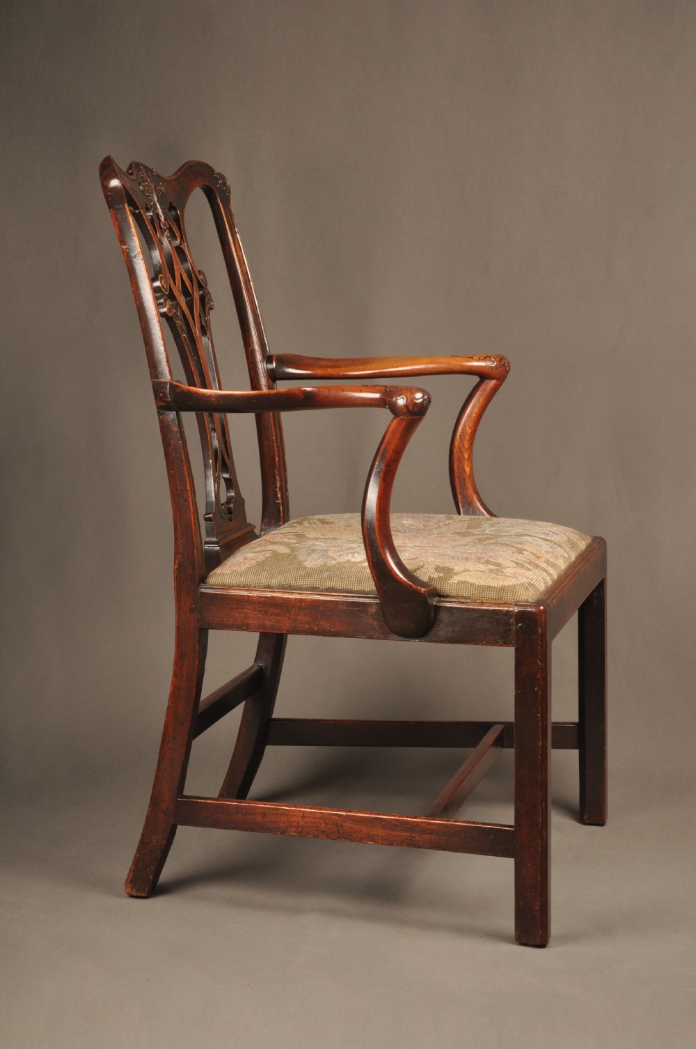 An 18th-century Chippendale mahogany armchair featuring a carved pierced splat back, swept armrests, an upholstered drop-in seat, and square legs joined by H-stretchers. View X