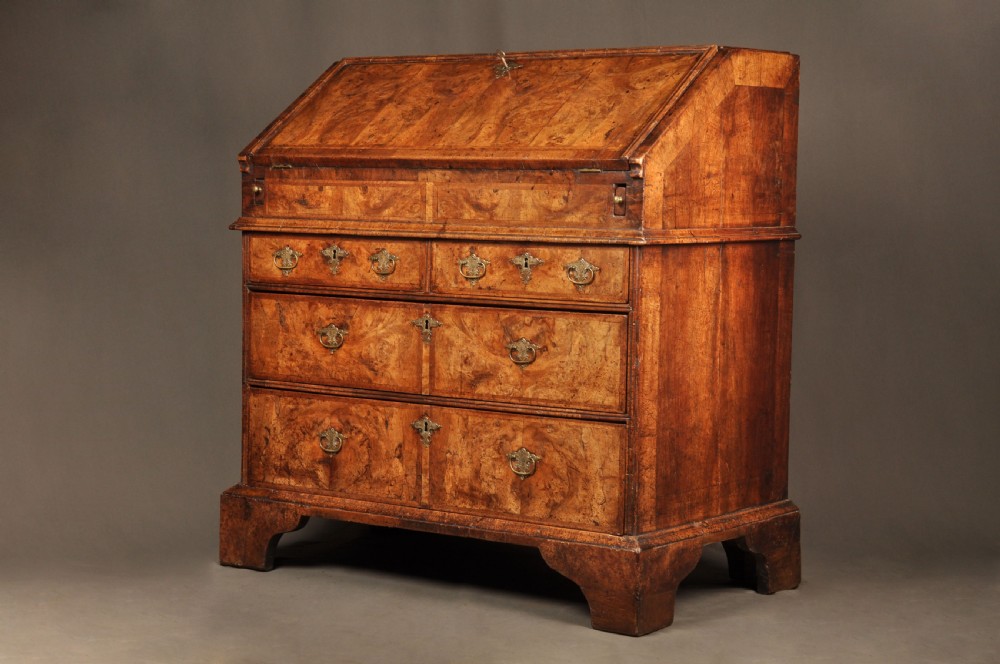 An eighteenth-century Queen Anne burr walnut bureau with a sloping fall-front lid above drawers featuring brass drop handles, resting on bracket feet. View II