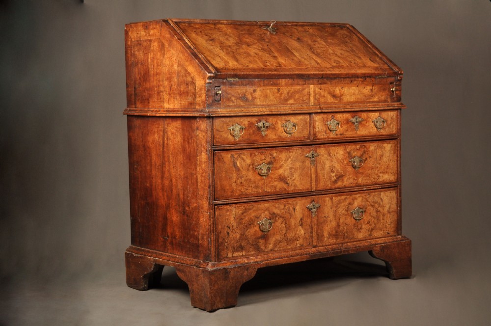 An eighteenth-century Queen Anne burr walnut bureau with a sloping fall-front lid above drawers featuring brass drop handles, resting on bracket feet. View III