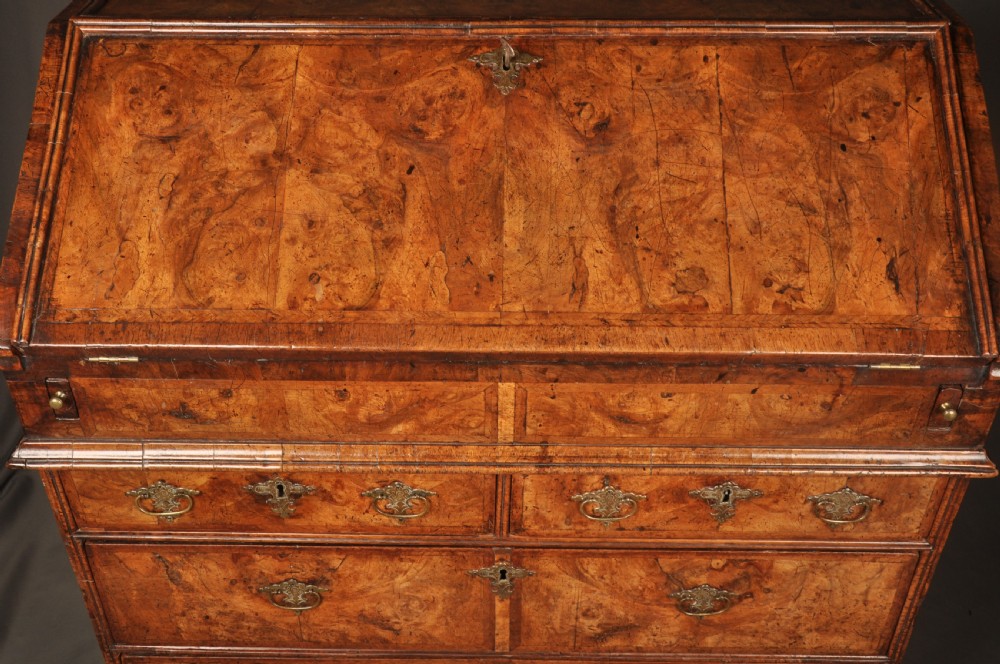 An eighteenth-century Queen Anne burr walnut bureau with a sloping fall-front lid above drawers featuring brass drop handles, resting on bracket feet. View VII