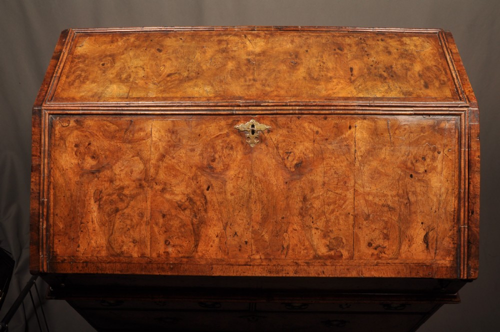 An eighteenth-century Queen Anne burr walnut bureau with a sloping fall-front lid above drawers featuring brass drop handles, resting on bracket feet. View XII