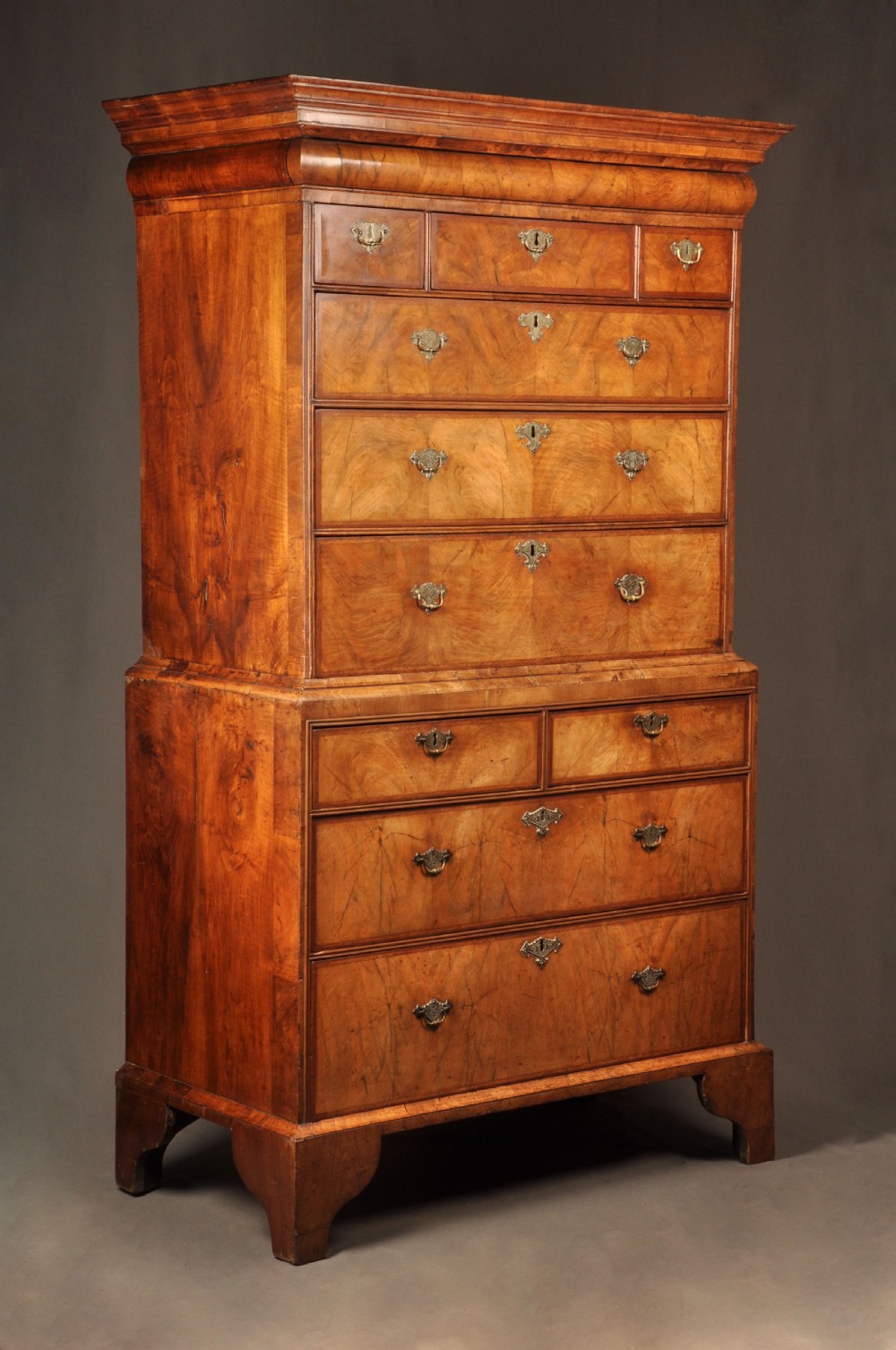 A tall Queen Anne walnut chest on chest featuring two stacked sections of drawers with brass handles and bracket feet.