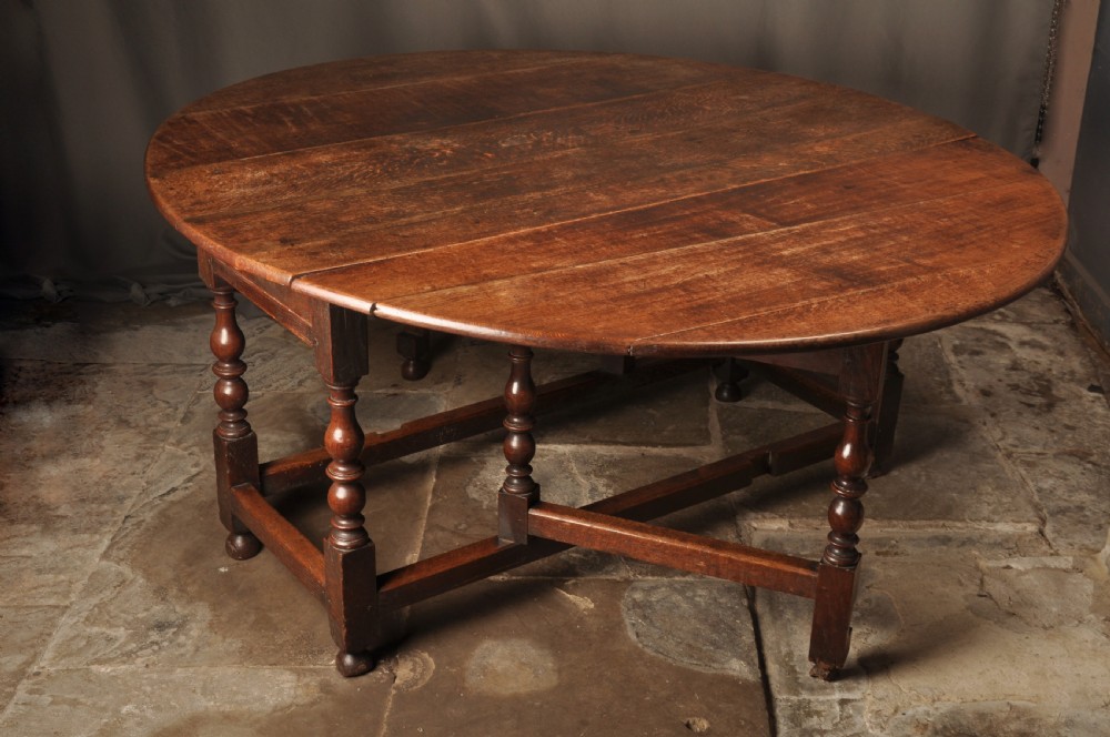 A large 17th-century solid oak gateleg dining table featuring drop leaves, turned legs, and perimeter stretchers.