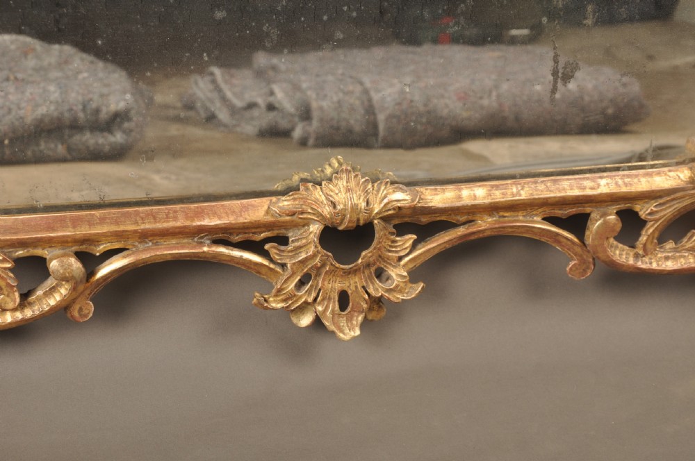 An 18th-century horizontal giltwood overmantel mirror featuring three glass plates set within a carved frame decorated with acanthus scrolls, C-scrolls, and floral motifs. View V