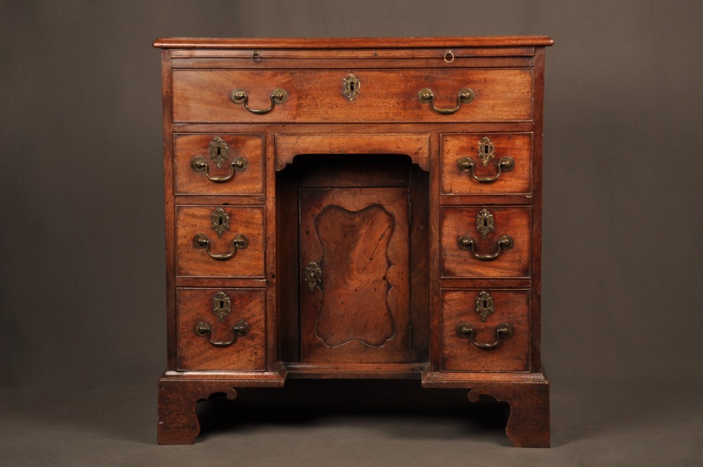 An 18th-century mahogany kneehole desk featuring a long upper drawer, six smaller side drawers, a central recessed cupboard, and bracket feet.