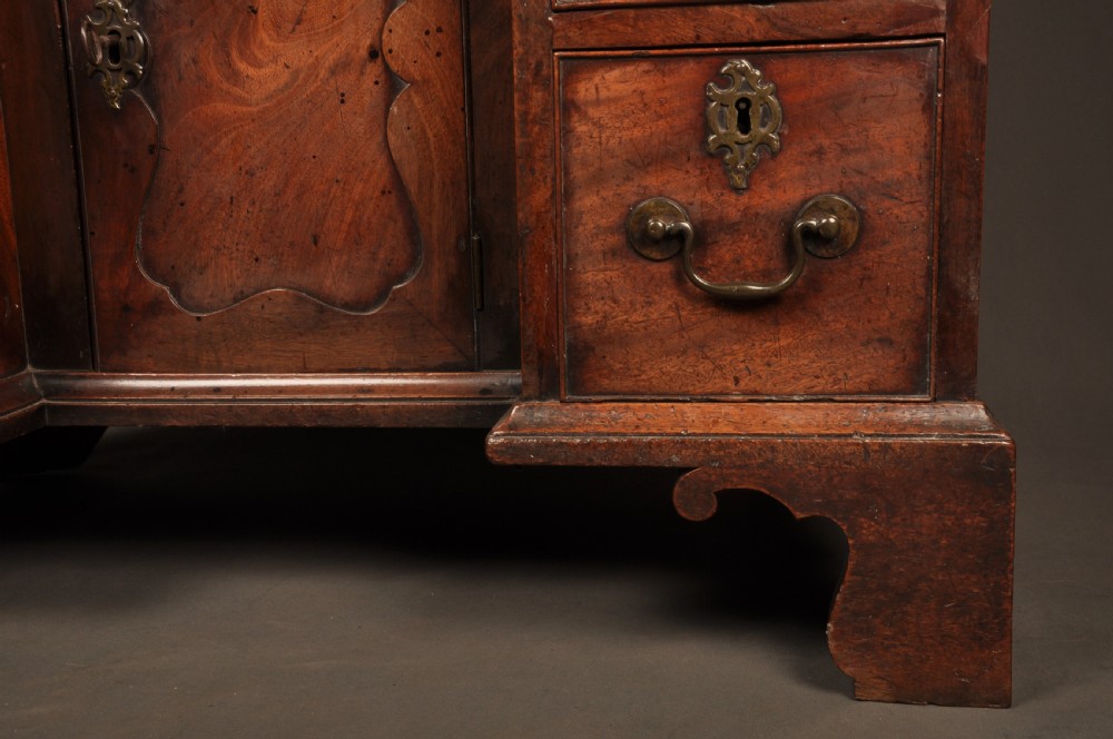 An 18th-century mahogany kneehole desk featuring a long upper drawer, six smaller side drawers, a central recessed cupboard, and bracket feet. View V