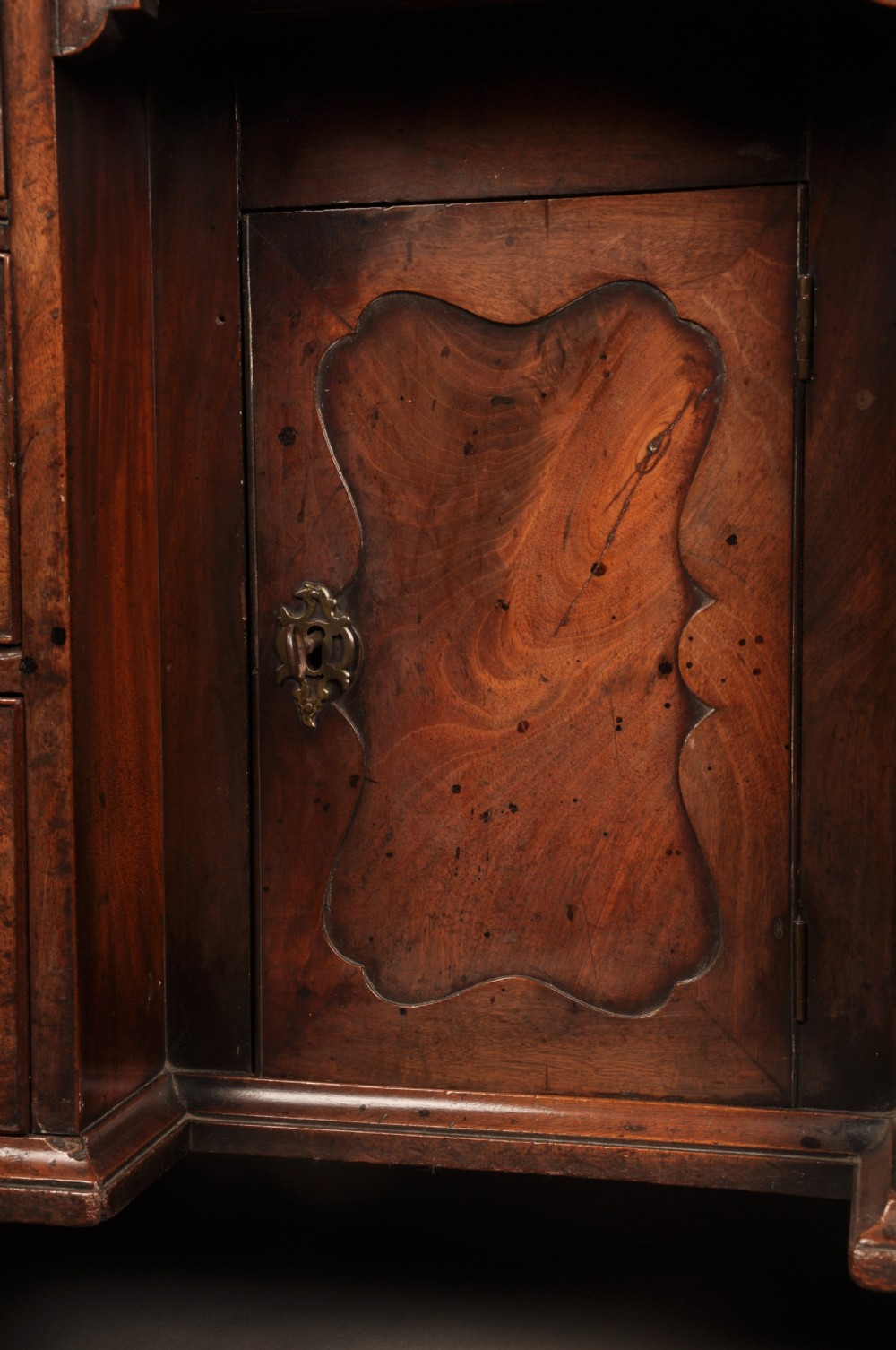 An 18th-century mahogany kneehole desk featuring a long upper drawer, six smaller side drawers, a central recessed cupboard, and bracket feet. View VI