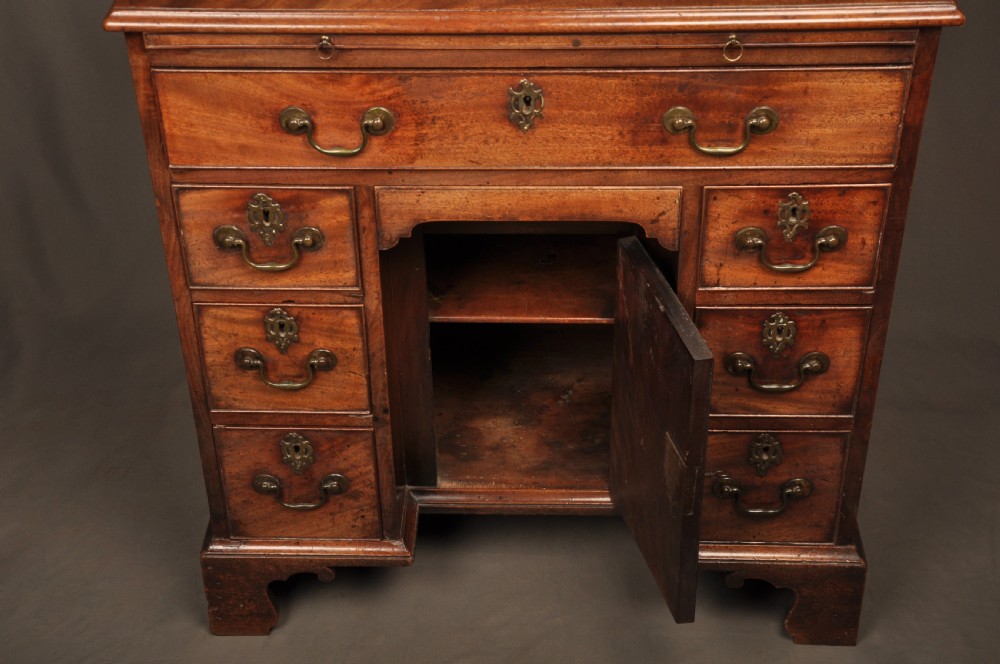 An 18th-century mahogany kneehole desk featuring a long upper drawer, six smaller side drawers, a central recessed cupboard, and bracket feet. View X