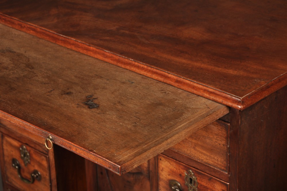 An 18th-century mahogany kneehole desk featuring a long upper drawer, six smaller side drawers, a central recessed cupboard, and bracket feet. View XVI