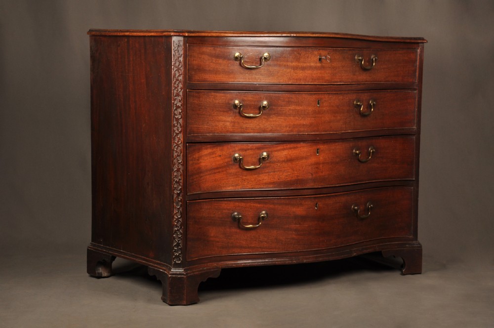 An 18th-century mahogany serpentine chest of drawers featuring four graduated drawers, carved canted corners, and brass swan-neck handles.