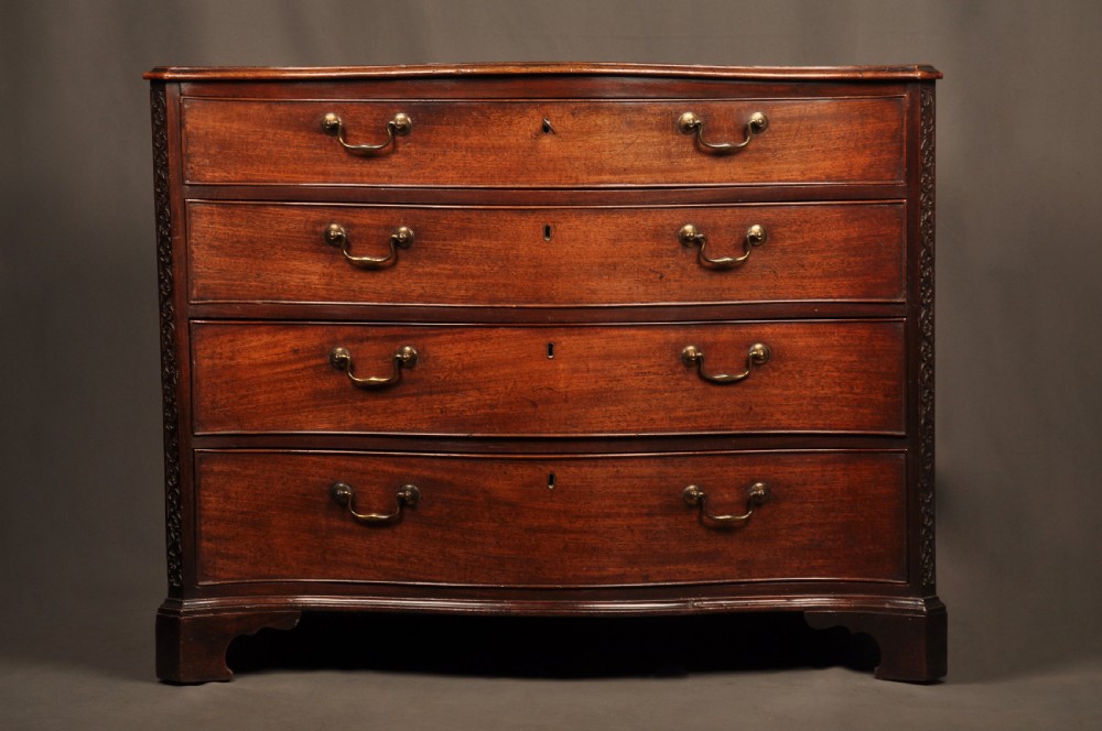 An 18th-century mahogany serpentine chest of drawers featuring four graduated drawers, carved canted corners, and brass swan-neck handles. View II