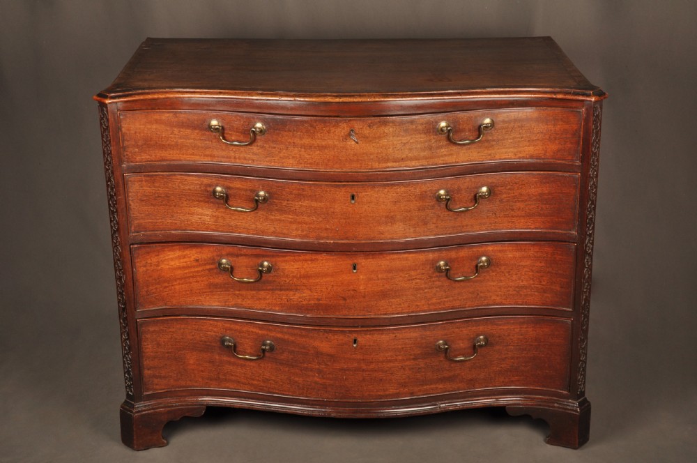 An 18th-century mahogany serpentine chest of drawers featuring four graduated drawers, carved canted corners, and brass swan-neck handles. View IV