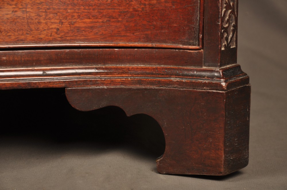 An 18th-century mahogany serpentine chest of drawers featuring four graduated drawers, carved canted corners, and brass swan-neck handles. View V