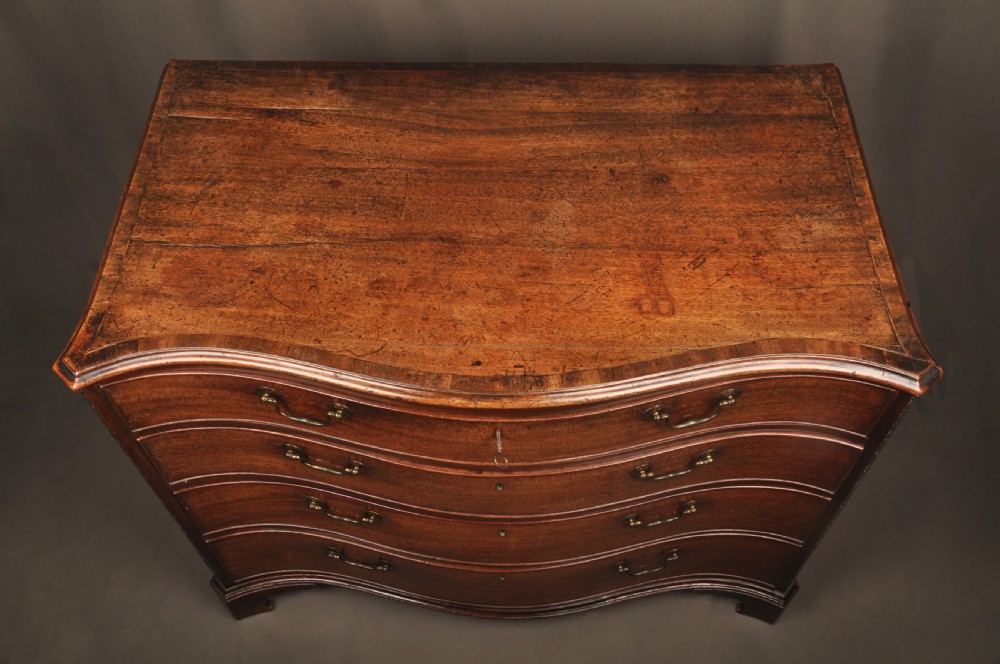 An 18th-century mahogany serpentine chest of drawers featuring four graduated drawers, carved canted corners, and brass swan-neck handles. View VIII