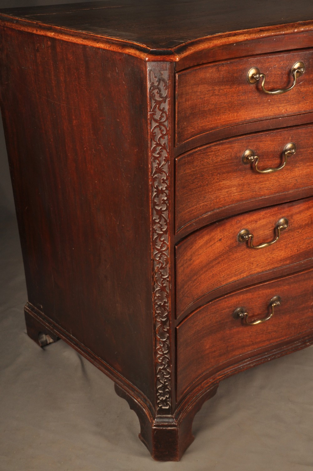 An 18th-century mahogany serpentine chest of drawers featuring four graduated drawers, carved canted corners, and brass swan-neck handles. View XI