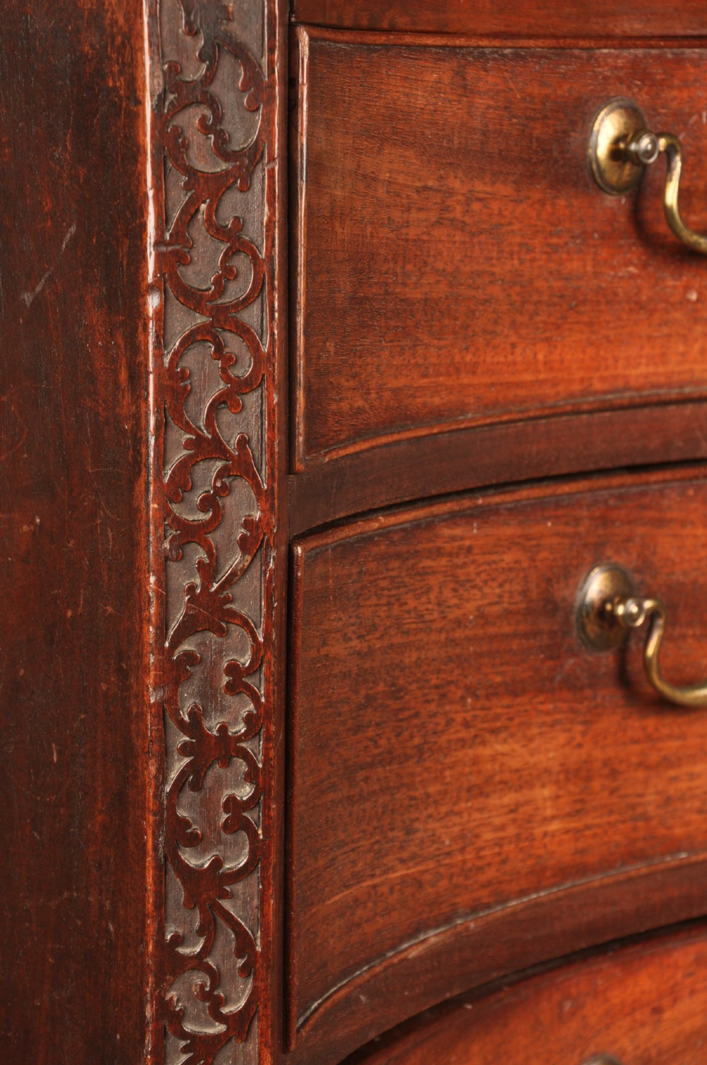 An 18th-century mahogany serpentine chest of drawers featuring four graduated drawers, carved canted corners, and brass swan-neck handles. View XII
