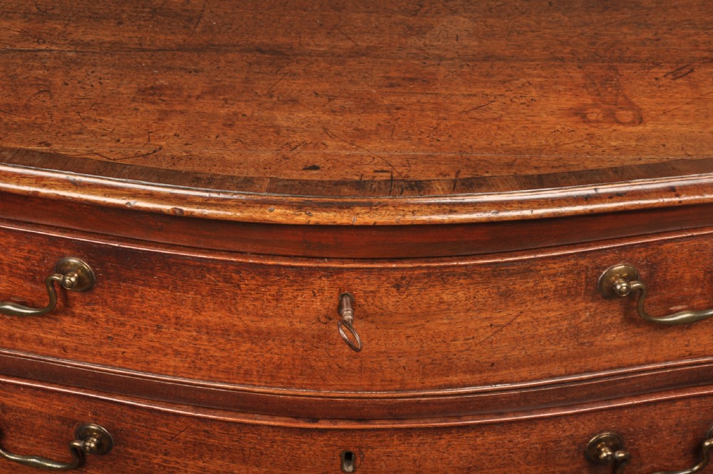An 18th-century mahogany serpentine chest of drawers featuring four graduated drawers, carved canted corners, and brass swan-neck handles. View XIII