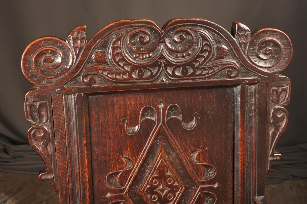A 17th-century dark oak wainscot armchair featuring a carved scroll cresting, lozenge-carved back panel, shaped armrests, and turned front legs. View III