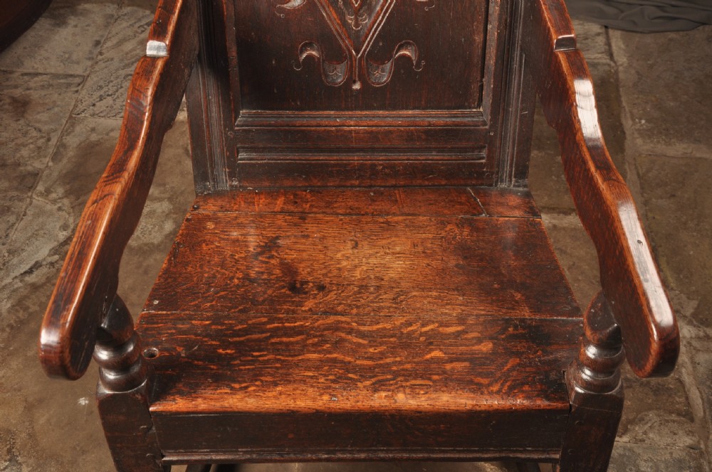 A 17th-century dark oak wainscot armchair featuring a carved scroll cresting, lozenge-carved back panel, shaped armrests, and turned front legs. View V