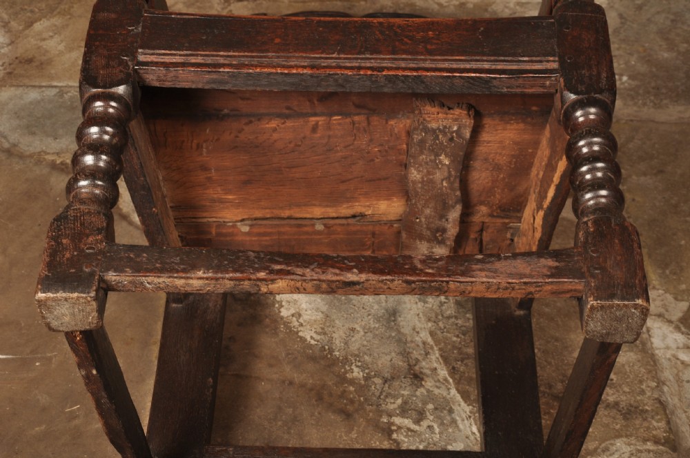 A 17th-century dark oak wainscot armchair featuring a carved scroll cresting, lozenge-carved back panel, shaped armrests, and turned front legs. View IX