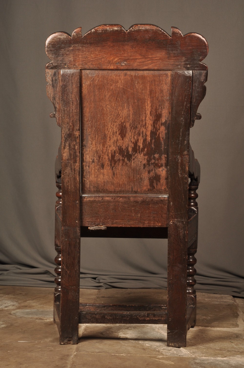 A 17th-century dark oak wainscot armchair featuring a carved scroll cresting, lozenge-carved back panel, shaped armrests, and turned front legs. View X
