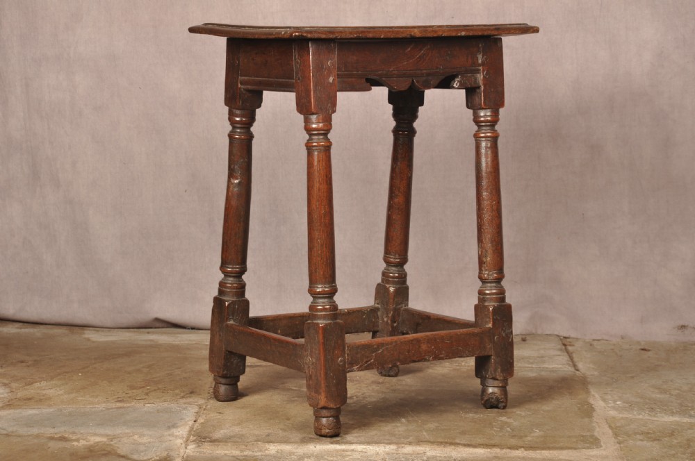 A mid-17th-century solid oak joint stool featuring turned legs, a rectangular top, and lower perimeter stretchers.