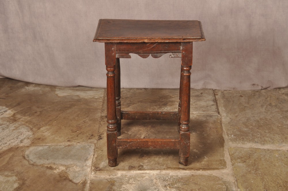 A mid-17th-century solid oak joint stool featuring turned legs, a rectangular top, and lower perimeter stretchers. View V