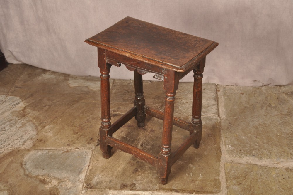 A mid-17th-century solid oak joint stool featuring turned legs, a rectangular top, and lower perimeter stretchers. View VI