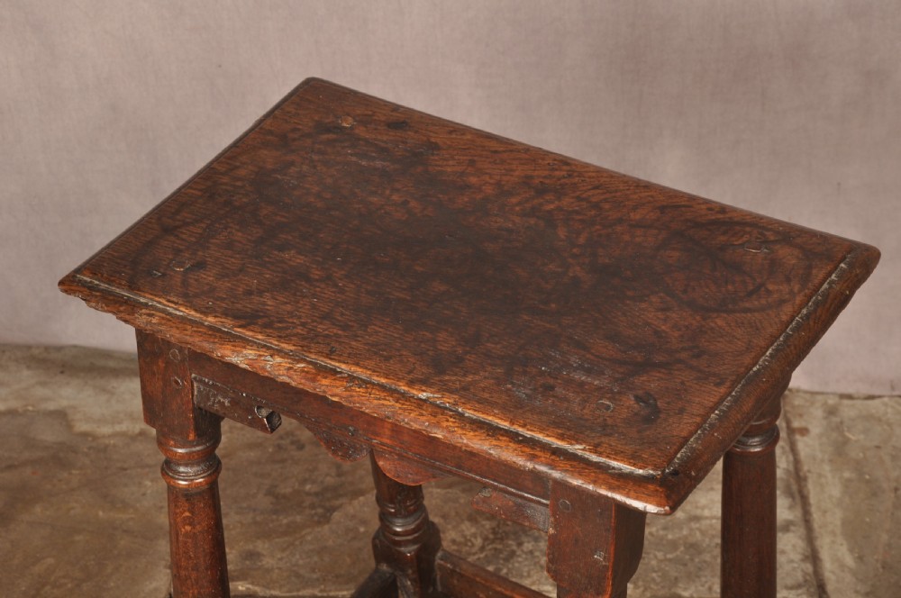 A mid-17th-century solid oak joint stool featuring turned legs, a rectangular top, and lower perimeter stretchers. View VII