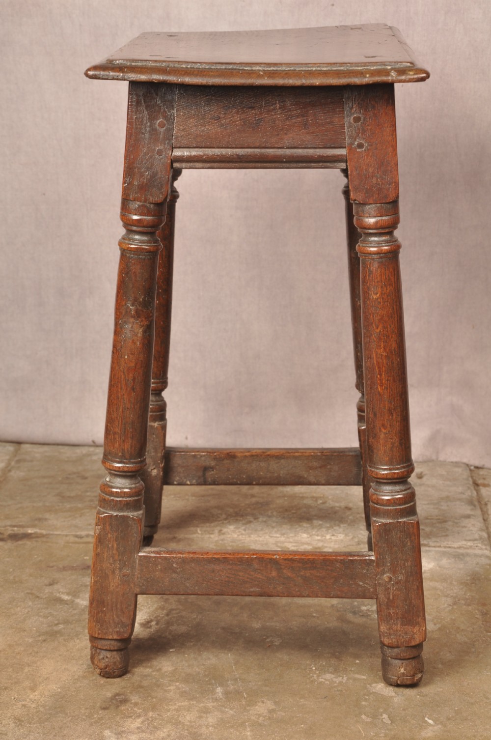 A mid-17th-century solid oak joint stool featuring turned legs, a rectangular top, and lower perimeter stretchers. View X